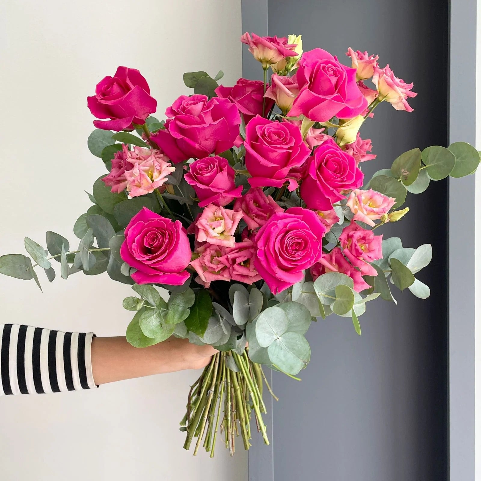 A lovely bouquet with hot pink roses, light champagne pink double-flowering lisianthus, and eucalyptus cinerea.